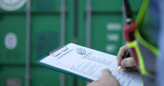 Handheld medium shot, Selective focus Hands of engineer man write on report paper on clipboard at storage container terminal