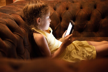 Little girl reads e-book lying on the couch late at night.