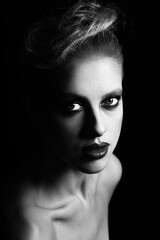 Fototapeta premium Make-up, hairstyle and fashion concept. Studio portrait of beautiful woman with fancy make-up and lipstick. Model looking at camera with seductive look in dark studio background. Black and white image