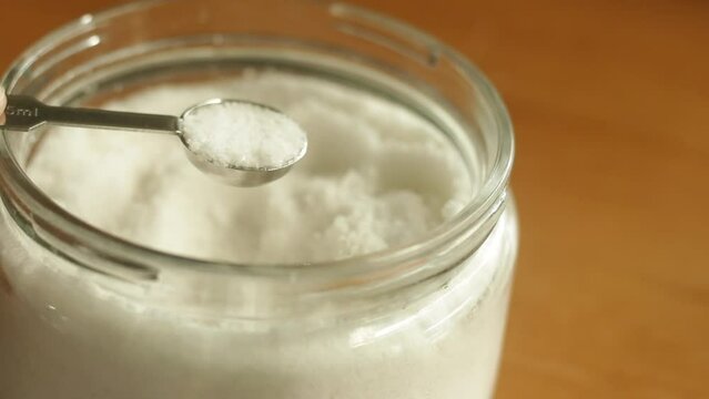A half teaspoon of table sea salt is being scooped with stainless steel measuring spoon cup