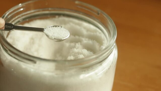 A quarter teaspoon of table sea salt is being scooped with stainless steel measuring spoon cup