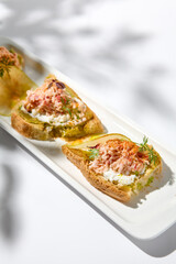 Aesthetic composition with crab bruschetta on white background with shadows from flowers. Italian bruschetta with crab, avocado and cheese on fine dining in summer. Elegant menu concept.