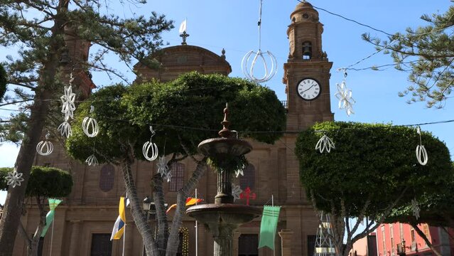 Cinematic shot of the fountain located in the Plaza de los Faycanes and at the bottom of the Galdar church and where flags can be seen waving on the masts. On the island of Gran Canaria.