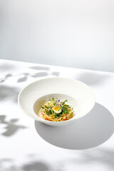 Healthy salad with squid and avocado on white plate with harsh shadows. Calamari salad with vegetables and eggs on white background with shadows of leaves. Summer food menu.