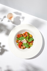 Salad with octopus, baked potatoes and poached egg on white table with hard shadows. Seafood salad with vegetables and potatoes in summer menu restaurant. Octopus and eggs salad in modern style.