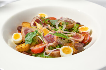 Traditional french salad nicoise with tuna, potatoes, eggs and vegetables on white table with harsh shadows. Tuna salad with quail eggs on white background with shadows of leaves.