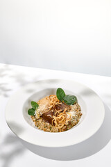 Elegant food - braised beef cheeks with buckwheat and gravy. Stew veal cheeks with sauce and green leaves in white plate with shadows. Summer style menu with hard shadows of leaves