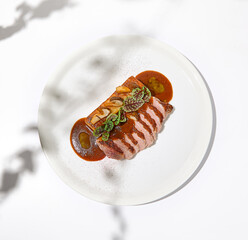 Roasted duck breast with potato gratin and sauce on light background. Fried duck fillet on white plate with hard shadows Elegant summer menu. French cuisine - duck breast with gravy