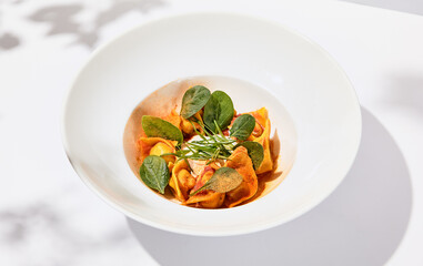 Tradition italian stuffed pasta - tortellini with minced meat. Italian ravioli on white background with harsh shadows. Summer menu italian restaurant. Tortellini with beef and spinach leaves