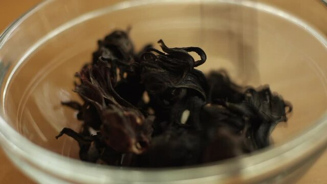A bunch of Dried purple Roselle flower fruits ( Jamaica sorrel, Rozelle or hibiscus sabdariffa ) are being poured to a clear glass bowl