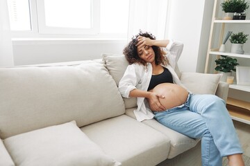 Pregnant woman headache lies at home in a shirt and jeans on the couch fatigue and heaviness in the last month of pregnancy before childbirth, motherhood difficulties, nausea