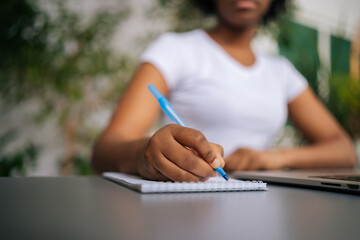 Close-up cropped shot of unrecognizable African-American woman holding pen writing working from...