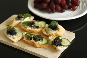 Bread appetizer with caviar, cucumber and mint leaves on a wooden board