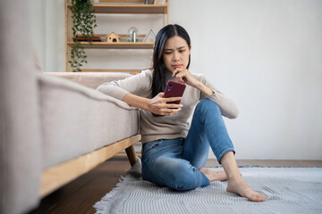 Portrait of beautiful young woman with depressed facial expression sitting holding her phone. Cyber bullying victim concept. Sad female in her room.