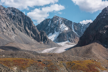 Obraz premium Scenic view to sunlit rocks and large snow mountain top with glacier in autumn sunny day. Vivid autumn colors in high mountains. Motley landscape with sharp rocks and snow mountain peak in bright sun.
