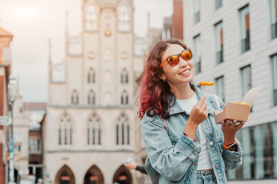 Cheerful happy girl snacking on fast food with shrimp in batter or french fries on the street of the city of Munster in Germany in a takeaway paper box