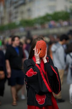 Vertical shot of a female in a Japanese costume holding a Tobi Obito resin mask on her face