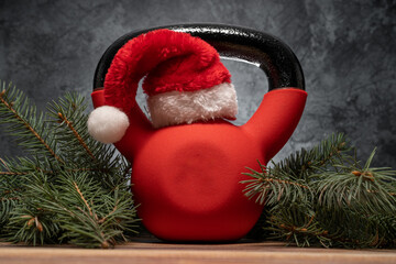 Heavy kettlebell in red Santa Claus hat. Exercise equipment as Christmas gift idea. Healthy fitness...