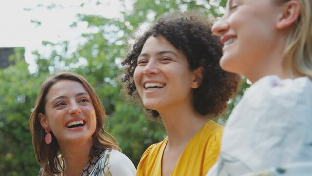 Three female friends sitting outdoors in summer garden at home relaxing and talking together - shot in slow motion 