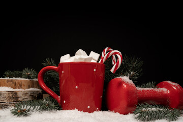 Hot chocolate or cocoa with marshmallows and candy canes, red dumbbell on white snow. Fitness...