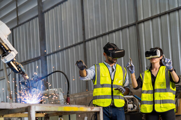 Male engineer and female working control robot arm system welding with VR glasses of virtual reality at production plant factory. Male and female worker control robot arm system welding by VR glasses - obrazy, fototapety, plakaty