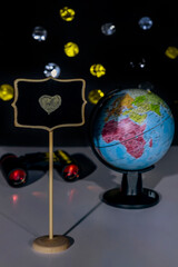 A yellow heart is drawn in chalk on a small blackboard with a globe and binoculars in the background