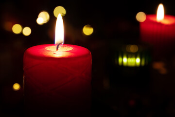 Burning red candle in the dark with other candles at the background and beautiful bokeh lights for a Christmas Eve celebration concept