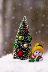 Miniature figurines of Christmas tree and a snowman in the snowy forest.