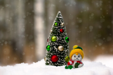 Miniature figurines of Christmas tree and a snowman in the snowy forest.