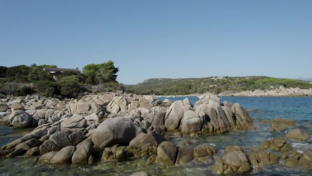 Rocky shore of Tizzano Beach in Corsica Island, Mediterranean Sea with boats and bathers, Aerial dolly in low shot

