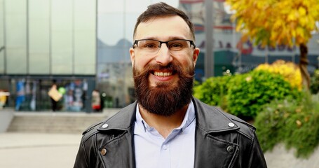 Portrait of the handsome Caucasian young man with long beard standing on the street and smiling.