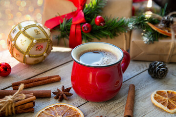 Christmas mood, holiday atmosphere. Red cup of coffee, Christmas gift boxes, Christmas tree golden ball, cones, star anise, cinnamon on a wooden windowsill.