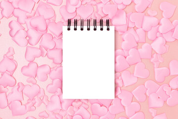 Blank notepad mockup and textile hearts confetti on a pink glittering background. Festive monochrome concept.