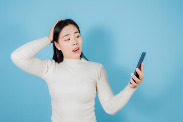 happy Asian woman holding mobile phone or smartphone on blue background