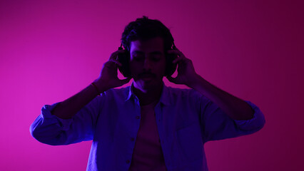 Young man listening to music isolated over purple background, chilling and enjoying music, headphones music concept