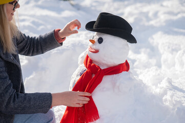 Caucasian woman sculpts a snowman from the snow. The carrot is the place of the nose.