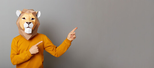 Photo of man with lion mask with wearing orange sweater, pointing away at advertisement area,...