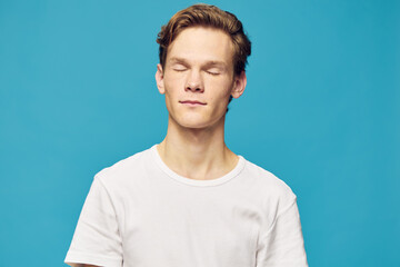 portrait of a guy in a white T-shirt with closed eyes on a blue background