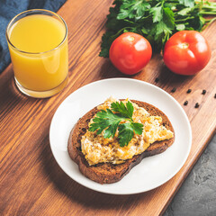 Scrambled eggs with parsley on bread at white plate, homemade healthy breakfast on wooden board