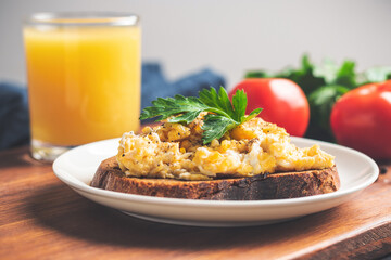 Scrambled eggs with parsley on bread at white plate, homemade healthy breakfast on wooden board