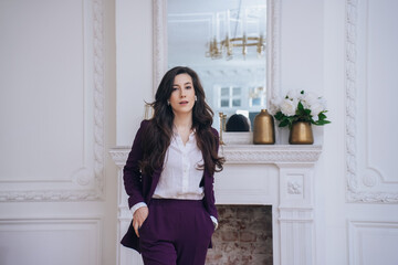 Purposeful Brunette Caucasian female entrepreneur in violet suit standing at home against classic interior with fireplace. Gorgeous Spanish businesswoman looks at camera. Business people.