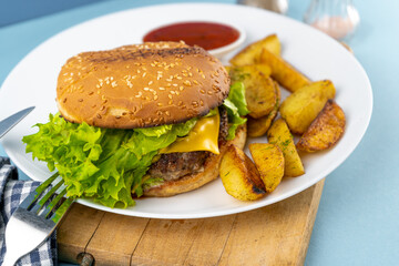 Homemade imperfect burger with potatoes and salad on a plate. Food on the table in a white plate on a wooden board