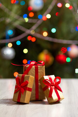 Gift boxes with red bows and blurred Christmas tree with twinkling party lights and toy balls.