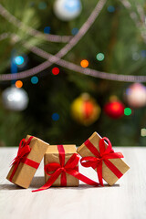 Gift boxes with red bows and blurred Christmas tree with twinkling party lights and toy balls.