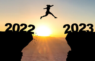 Woman jumps over abyss with sunset in background and inscription 2022 and 2023