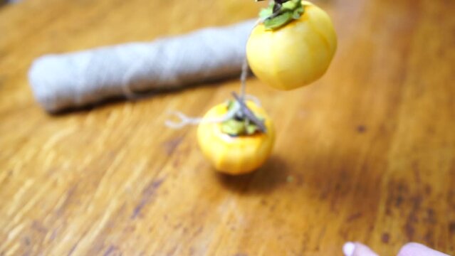 Woman hands preparing fresh persimmon fruit for drying, lined up on a rope. Row of Hanging Japanese dried Persimmon - Hoshigaki on strings to preserved it in autumn season. Selective focus