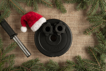 Heavy dumbbells barbell weight plate disc in a red Santa Claus Christmas hat. Healthy fitness...