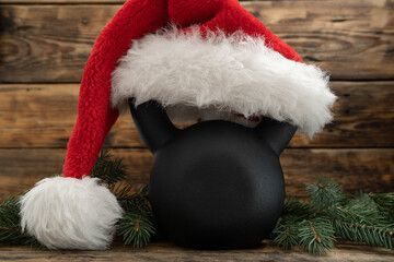 Heavy kettlebell in red Santa Claus hat. Exercise equipment as Christmas gift idea. Healthy fitness lifestyle holiday season winter composition. Gym workout and sport training concept.