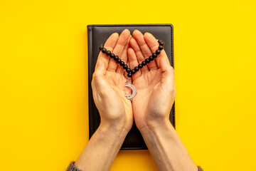 Praying hands hold black Muslim rosary with silver crescent moon