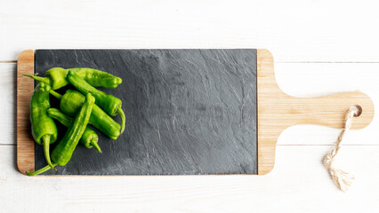 Green peppers on slate plate on white wooden background